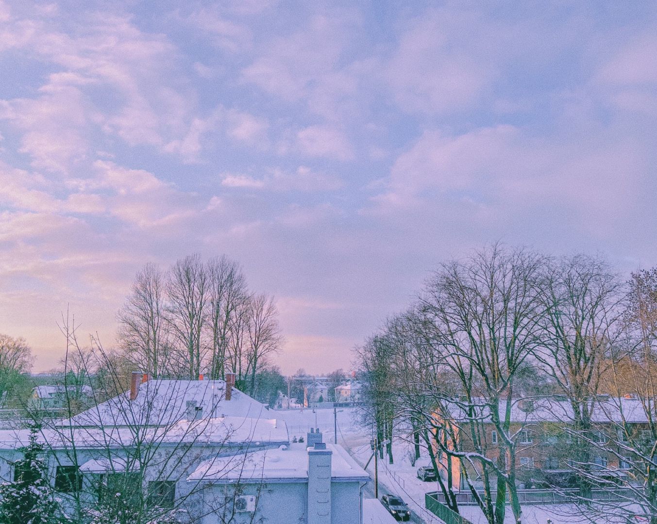 view on snow covered houses, a street and trees. the sunset makes the scene look soft.