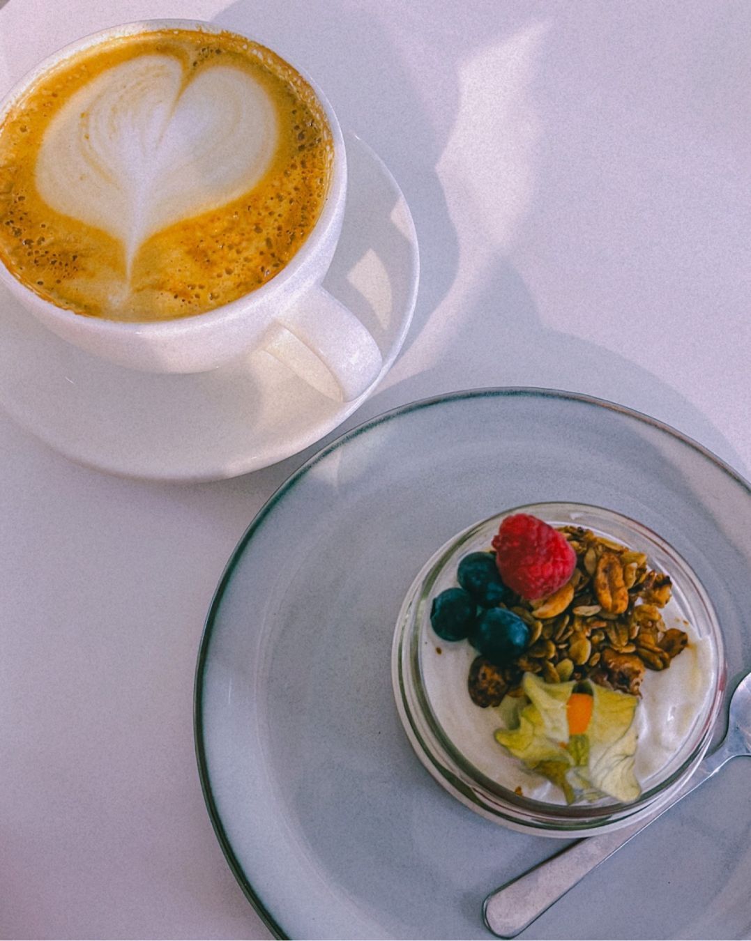 a cup of coffee and a glass with yoghurt, berries and oats.