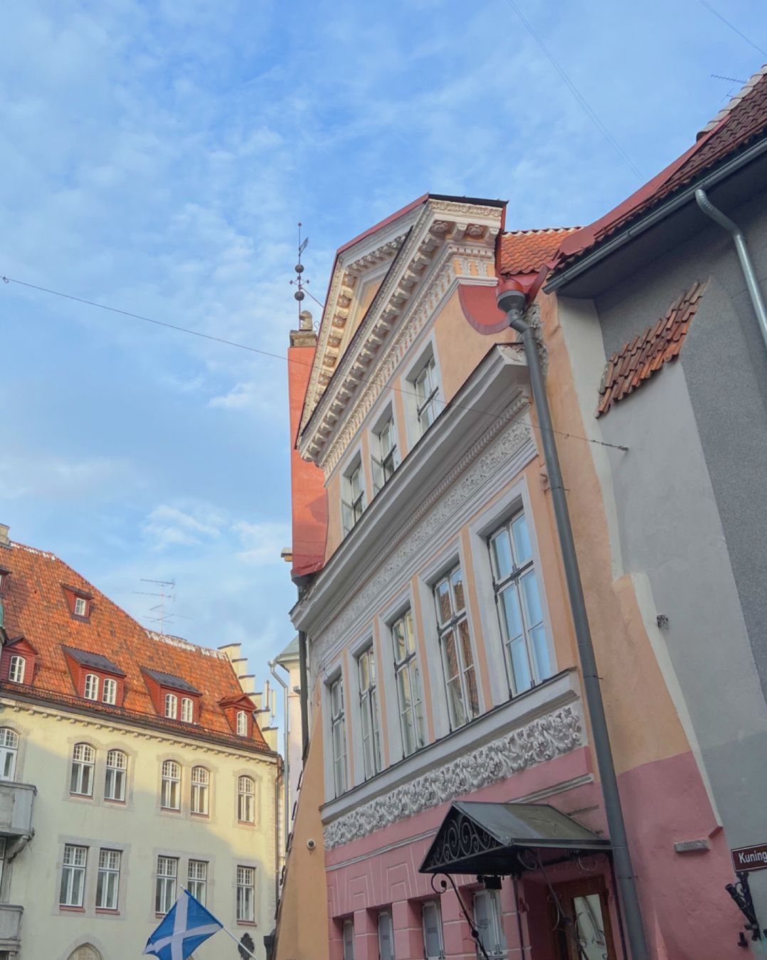 houre fronts in pastel yellow with a bit of pastel pink, and a red roof. the sky is blue with just a bit of clouds.